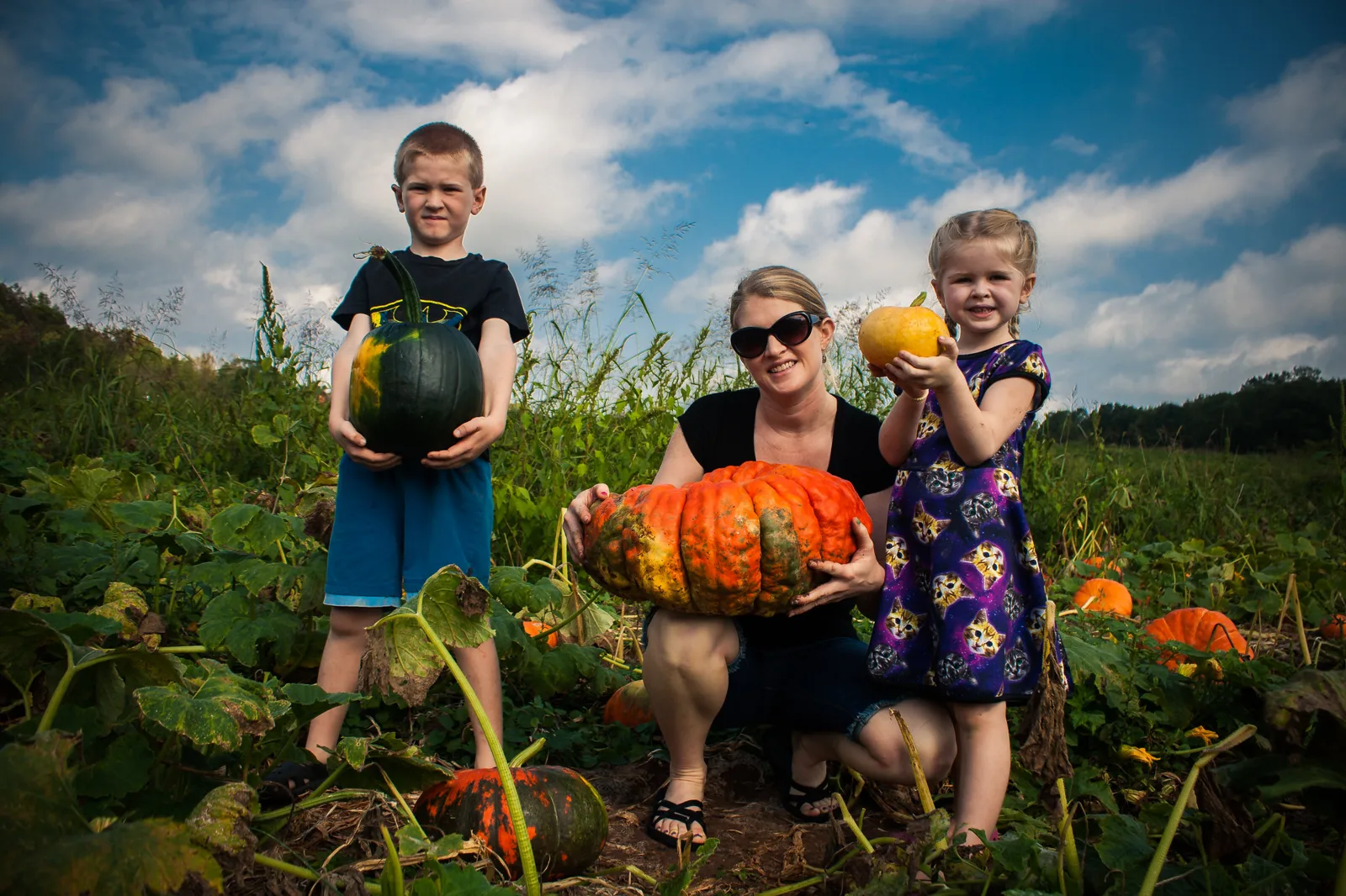 A family holds up pumpkins picked in a pumpkin field.